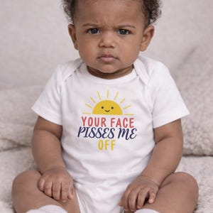 May include: A white baby onesie with the text "YOUR FACE PISSES ME OFF" in yellow, red, and blue. The onesie features a smiling sun graphic. A baby with a serious expression is wearing the onesie.