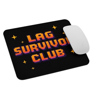 Peut inclure: Tapis de souris rectangulaire noir aux coins arrondis. Le tapis affiche le texte "LAG SURVIVOR CLUB" en lettres pixelisées orange et violettes. Une souris sans fil blanche est positionnée à droite. De petites étoiles et des symboles plus jaunes sont dispersés.