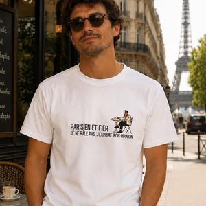 Può includere: T-shirt bianco con la scritta "PARISIEN ET FIER JE NE RALE PAS, J'EXPRIME MON OPINION" e una grafica di una persona a un tavolino di un caffè. La Torre Eiffel è visibile sullo sfondo.