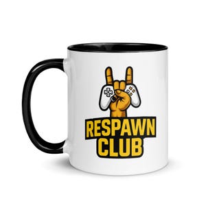 May include: White ceramic mug with a black interior and handle. The mug features a graphic of a hand making a rock-and-roll gesture, holding a video game controller. The text "RESPAWN CLUB" is displayed in yellow.