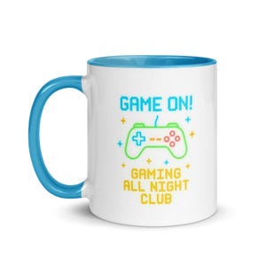 May include: White ceramic mug with a blue handle and interior. The mug features the text "GAME ON!" above a neon green and red controller graphic, with the words "GAMING ALL NIGHT CLUB" below.