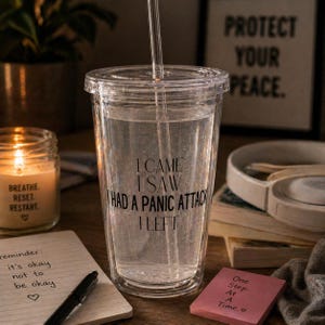 Peut inclure: Un gobelet transparent à double paroi avec une paille, rempli de liquide. Le gobelet porte l'inscription "I CAME I SAW HAD A PANIC ATTACK I LEFT". Une bougie et un bloc-notes sont en arrière-plan.