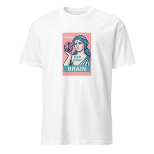 Peut inclure: Un t-shirt blanc avec un motif rectangulaire sur la poitrine. L'illustration représente une figure de style classique aux cheveux bleus tenant un cerveau sur un fond rose. Le texte indique : PLEASE use your BRAIN en lettres bleues et blanches.