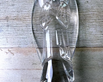 Könnte beinhalten: Eine transparente Glasengel-Figur mit ausgebreiteten Flügeln. Der Engel hält die Hände vor der Brust zusammen. Auf dem Sockel der Figur ist das Wort "Baccarat" eingraviert. Der Engel steht auf einer Holzoberfläche.