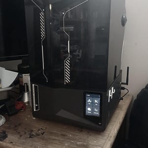 Könnte beinhalten: Ein schwarzer 3D-Drucker mit einem Touchscreen-Display und zwei Antennen. Der Drucker steht auf einem Holztisch.