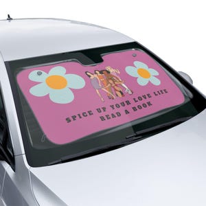 May include: Pink car sunshade with a graphic of five women, two blue and yellow flowers, and the text "Spice up your love life read a book".