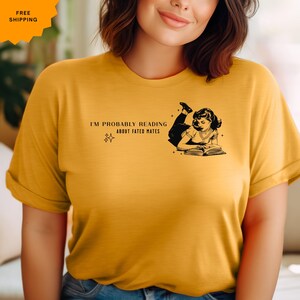 May include: A yellow t-shirt with a black graphic of a woman reading a book. The text on the shirt reads "I'm probably reading about fated mates."