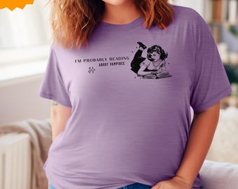 May include: A purple t-shirt with a graphic of a woman reading a book. The text on the shirt reads "I'm probably reading about vampires."