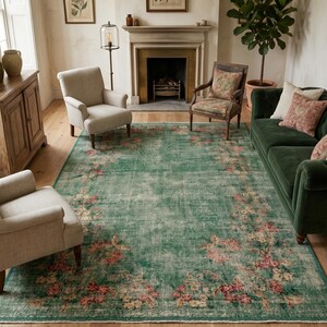 May include: A large, rectangular, distressed green rug with a floral pattern in pink and cream. The rug is placed in a living room with a green sofa, two armchairs, and a wooden cabinet. The room has a fireplace and framed botanical prints.