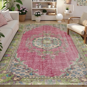 Puede incluir: Una alfombra rectangular grande con un aspecto vintage y desgastado. La alfombra presenta un diseño de medallón central en color turquesa y crema sobre un fondo rosa descolorido. El borde es una mezcla de verde, azul y crema.