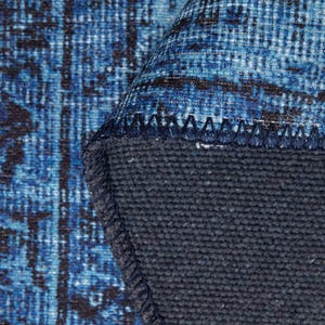 May include: Close-up of a rolled-up blue and black patterned rug. The rug's design features a distressed, vintage aesthetic with a dark blue backing. The edges are neatly stitched, showcasing the rug's construction.