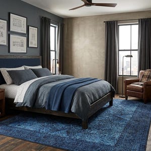 May include: A bedroom with a dark blue rug, a bed with blue bedding, and a brown leather armchair. The room has dark gray curtains, a wooden dresser, and framed architectural drawings on the wall.