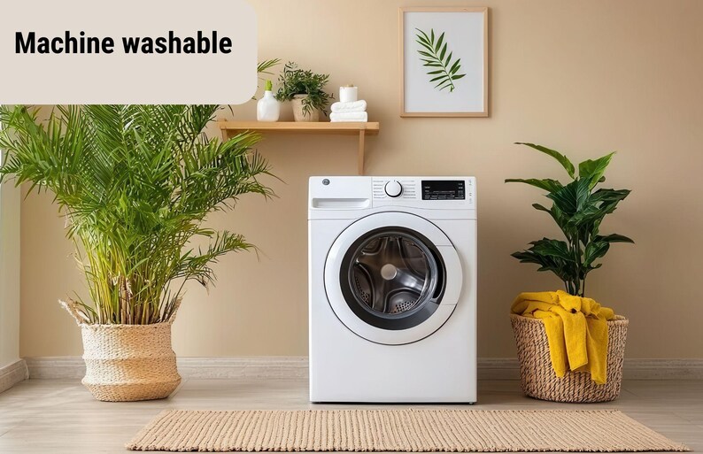 May include: A white washing machine with a black control panel is centered in a room. The text "Machine washable" is in the upper left. Potted plants and a framed botanical print decorate the space. A woven rug is on the floor.