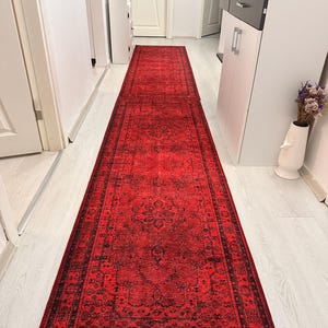 Könnte beinhalten: Ein langer, rechteckiger roter Teppich mit einem komplizierten schwarzen Muster. Der Teppich befindet sich in einem Flur und zeigt ein traditionelles Design mit floralen und geometrischen Motiven. Die satte Farbe und das detaillierte Design des Teppichs verleihen dem Raum einen Hauch von Eleganz.