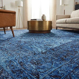 May include: A large, blue area rug with a distressed, patterned design. The rug features shades of blue and black, creating a vintage look. The rug is placed in a living room setting with furniture.
