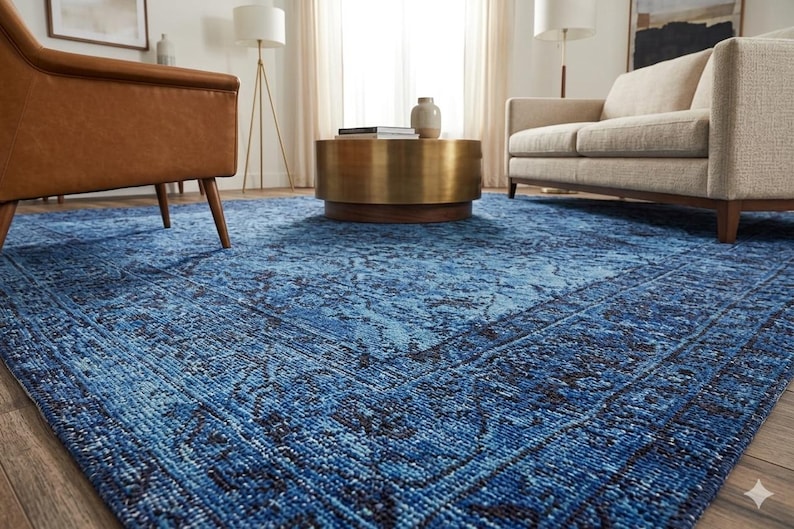 May include: A large, blue area rug with a distressed, patterned design. The rug features shades of blue and black, creating a vintage look. The rug is placed in a living room setting with furniture.