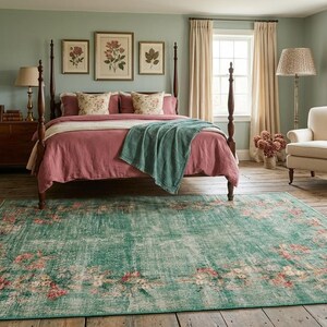 May include: A bedroom with a four-poster bed, a patterned rug, and framed botanical prints. The bed has a dusty rose comforter and a teal throw. The rug is teal with a floral pattern. A wooden armoire and a cream-colored armchair are also present.