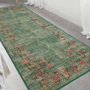 May include: A rectangular green rug with a floral pattern in shades of pink, beige, and red. The rug has a distressed, vintage look and a dark green border. The floral design is concentrated along the edges.