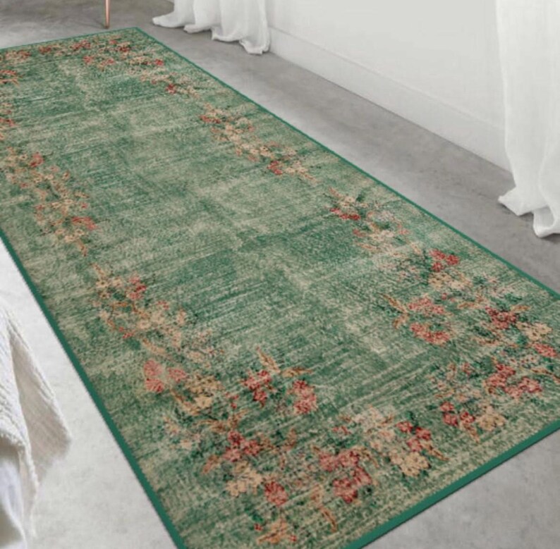 May include: A rectangular green rug with a floral pattern in shades of pink, beige, and red. The rug has a distressed, vintage look and a dark green border. The floral design is concentrated along the edges.