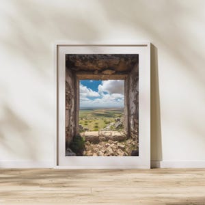 May include: A framed photograph of a view through a window in a stone building. The view shows a green field with a blue sky and white clouds.