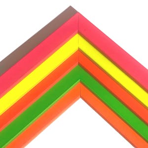 May include: A corner section of a multi-layered picture frame featuring five distinct angled strips. The colors arranged from the outermost to the innermost layer are brown, neon pink, bright yellow, orange, and a vibrant lime green.