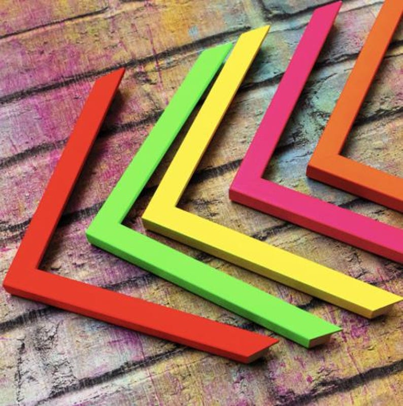 May include: Four L-shaped picture frame corners in vibrant neon colors. The set includes one red, one lime green, one yellow, and one hot pink corner piece, each featuring a flat, smooth surface and angled edges for joining together.