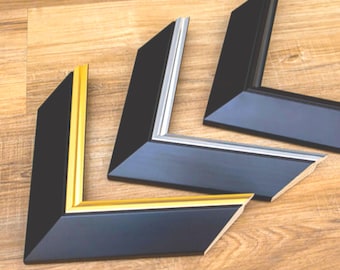 Könnte beinhalten: Drei schwarze Bilderrahmen-Ecken mit unterschiedlichen Innenfarben: Gold, Silber und Schwarz. Die Rahmen sind abgewinkelt und haben eine abgeschrägte Kante. Der Hintergrund ist eine hellbraune Holzoberfläche.