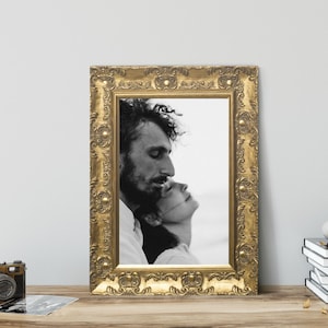 Op de afbeelding: Een rechthoekige fotolijst met een sierlijke, reli&euml;f gouden afwerking met een zwart-witfoto van twee mensen die tegen elkaar aan leunen. De lijst is voorzien van ingewikkeld krulwerk en verhoogde cirkelvormige details langs de rand.