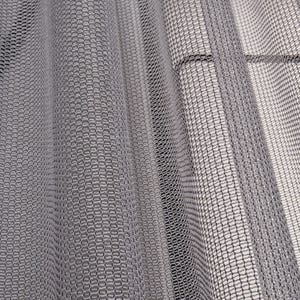 May include: Close-up of a gray, textured fabric with a repeating pattern. The fabric is draped, creating soft folds and shadows. The material appears to be a fine mesh or net-like weave, suitable for curtains or decorative purposes.