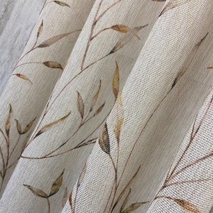 Könnte beinhalten: Ein halbtransparenter Vorhang aus gewebtem, strukturiertem Stoff in einem Off-White- oder Cremeton. Der Vorhang ist mit einem zarten, sich wiederholenden botanischen Druck aus dünnen, braunen und goldfarbenen Zweigen mit kleinen Blättern verziert.