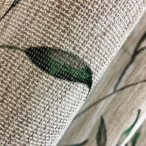 Könnte beinhalten: Ein strukturierter Stoff mit ausgeprägtem Gewebe, der ein Druckmuster aus dunkelgrünen Blättern und dünnen braunen Stielen aufweist. Das Material hat eine hellbeige Grundfarbe und eine sichtbare gitterartige Struktur in Nahaufnahme.