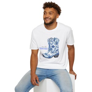Op de afbeelding: Wit T-shirt met een blauwe en witte cowboylaars met bloemenprint en de tekst "Not old. Vintage."