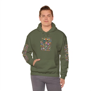 Op de afbeelding: Een groene hoodie met een kleurrijke bloemenprint op de voorkant en mouwen. De print bevat een verscheidenheid aan bloemen en bladeren in tinten roze, paars, blauw, geel en oranje.