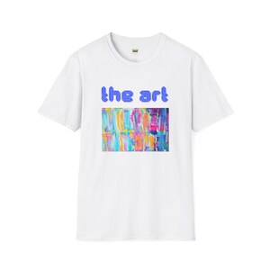 Op de afbeelding: Wit T-shirt met een kleurrijk abstract schilderij en de tekst "the art" in blauw.
