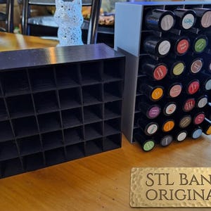 May include: Black and gray 3D-printed storage organizers. One is a grid of small square compartments, the other holds coffee pods. The sign reads "STL BANK ORIGINAL".