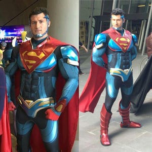 May include: A Superman costume in blue and black with red and gold details. The chest displays the Superman "S" emblem. The outfit includes a red cape, blue boots, and a headpiece. The person is standing outside.