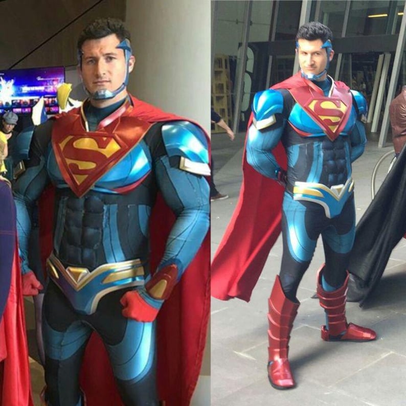 May include: A Superman costume in blue and black with red and gold details. The chest displays the Superman "S" emblem. The outfit includes a red cape, blue boots, and a headpiece. The person is standing outside.