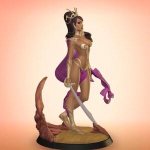 Puede incluir: Figura de fantas&iacute;a de una mujer con capa morada y armadura dorada, sosteniendo una espada. La figura se alza sobre una base con textura arenosa y borde oscuro. La mujer tiene cabello oscuro y est&aacute; adornada con joyas.