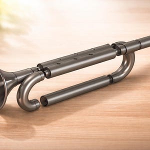 Può includere: Uno strumento musicale grigio metallizzato smontato, forse una tromba o uno strumento a fiato simile, è appoggiato su una superficie di legno. Lo strumento presenta una campana svasata, tubi curvi e un bocchino. Il design suggerisce un'estetica moderna.