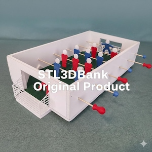 May include: A miniature foosball table with a white exterior, green playing surface, and red and blue player figures. The table has wooden rods with red and blue handles. The text "STL3DBank Original Product" is visible on the side.