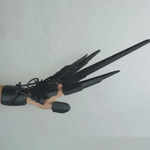 以下が含まれることがあります： 指先から伸びる4つの長く鋭い刃が付いた黒い爪付き手袋。手袋は手首の袖口と指なしのデザインが特徴で、革紐で接続されています。ブレードは角度が付けられており、硬い素材でできているようです。