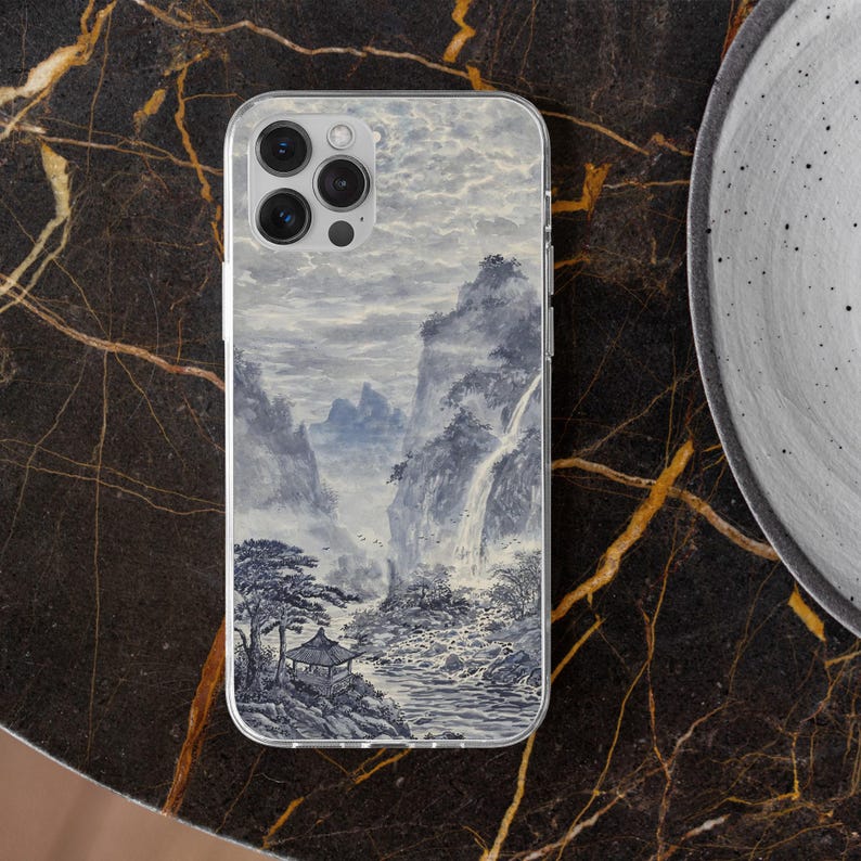 Pu&ograve; includere: Custodia trasparente per telefono con un design paesaggistico nei toni del grigio e del blu. L'opera d'arte raffigura montagne, cascate e un padiglione in stile asiatico. La custodia &egrave; esposta su una superficie di marmo scuro.