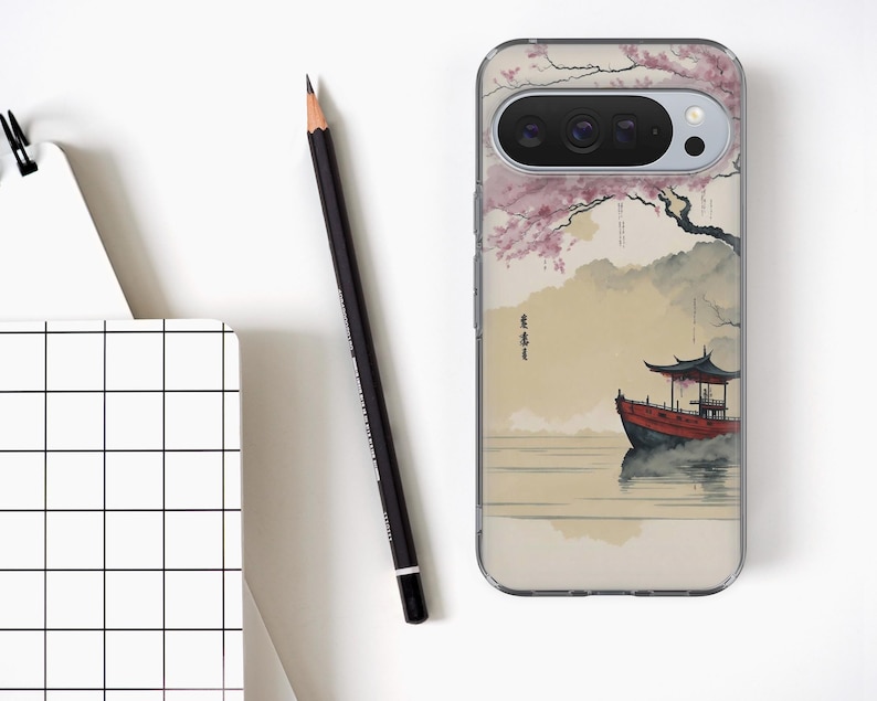 May include: Clear phone case featuring a Japanese-style painting of a red boat on water, with a pagoda and cherry blossom tree. The case has a black camera lens and a clear border. A black pencil and a notepad with a grid pattern are also in the image.
