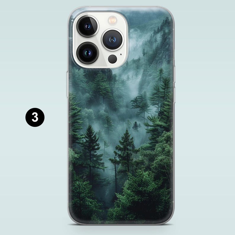 May include: A phone case with a misty forest scene. The image features a lush green forest with fog rolling through the trees. The phone case is clear and shows the phone's camera lens.