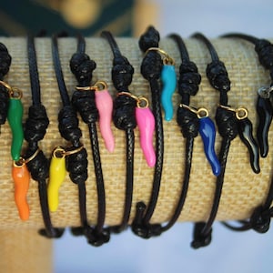 Op de afbeelding: Een verzameling zwarte armbandjes van touw met kleurrijke hoornvormige bedels. De bedels zijn in verschillende kleuren, waaronder groen, roze, geel, blauw en zwart.