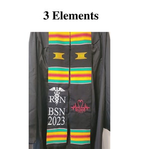 May include: Black graduation stole with colorful stripes of green, yellow, and red. The stole features white text that reads "R N BSN 2023" and a caduceus symbol. Another section has a pink heart symbol and the text "&Delta;&Sigma;&Theta; 2023". The words "3 Elements" are at the top.