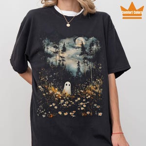 Puede incluir: Camiseta negra con una escena de bosque con un fantasma, árboles y una luna llena. La camiseta tiene el texto "Comfort Colors" y "Color: Black".