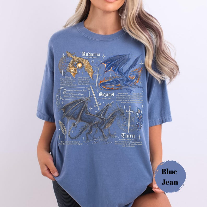 May include: A blue short-sleeve t-shirt featuring a detailed graphic print of three dragons labeled Andarna, Sgaeyl, and Tairn. The design includes intricate illustrations of swords, feathers, and text descriptions in a vintage style font.