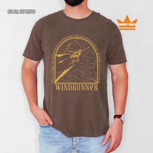 Puede incluir: Camiseta color espresso con un gr&aacute;fico dorado de una figura y el texto "WINDRUNNER". La camiseta tambi&eacute;n presenta las frases "LIFE BEFORE DEATH, STRENGTH BEFORE WEAKNESS, JOURNEY BEFORE DESTINATION". Marca Comfort Colors.