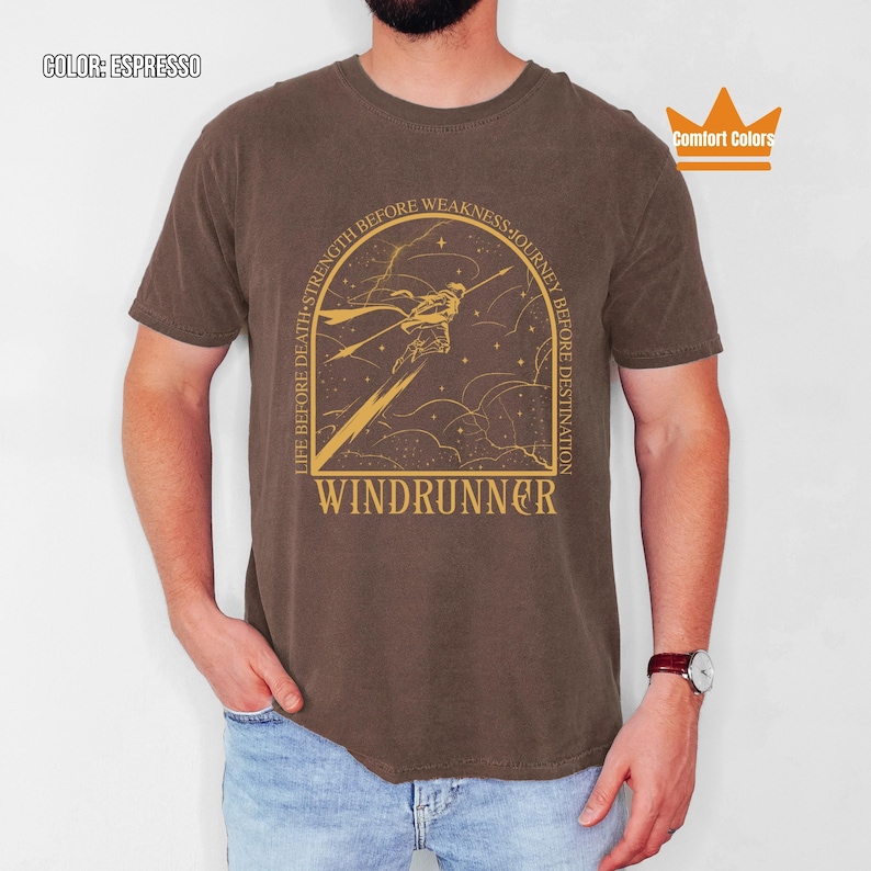 Puede incluir: Camiseta color espresso con un gr&aacute;fico dorado de una figura y el texto "WINDRUNNER". La camiseta tambi&eacute;n presenta las frases "LIFE BEFORE DEATH, STRENGTH BEFORE WEAKNESS, JOURNEY BEFORE DESTINATION". Marca Comfort Colors.